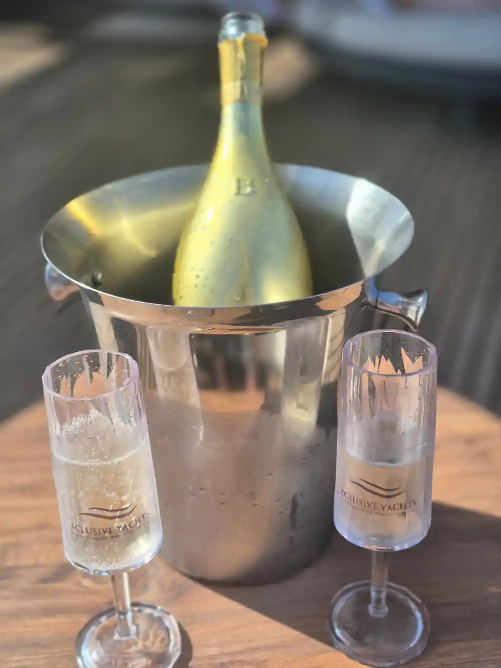 A bottle in an ice bucket with branded glasses on deck