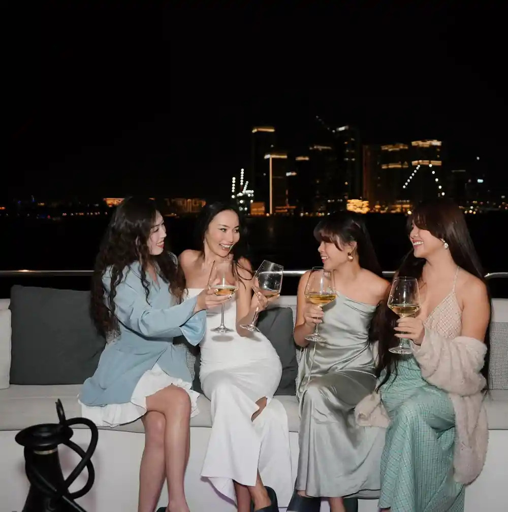 Guests with wine glasses on deck at night, skyline behind
