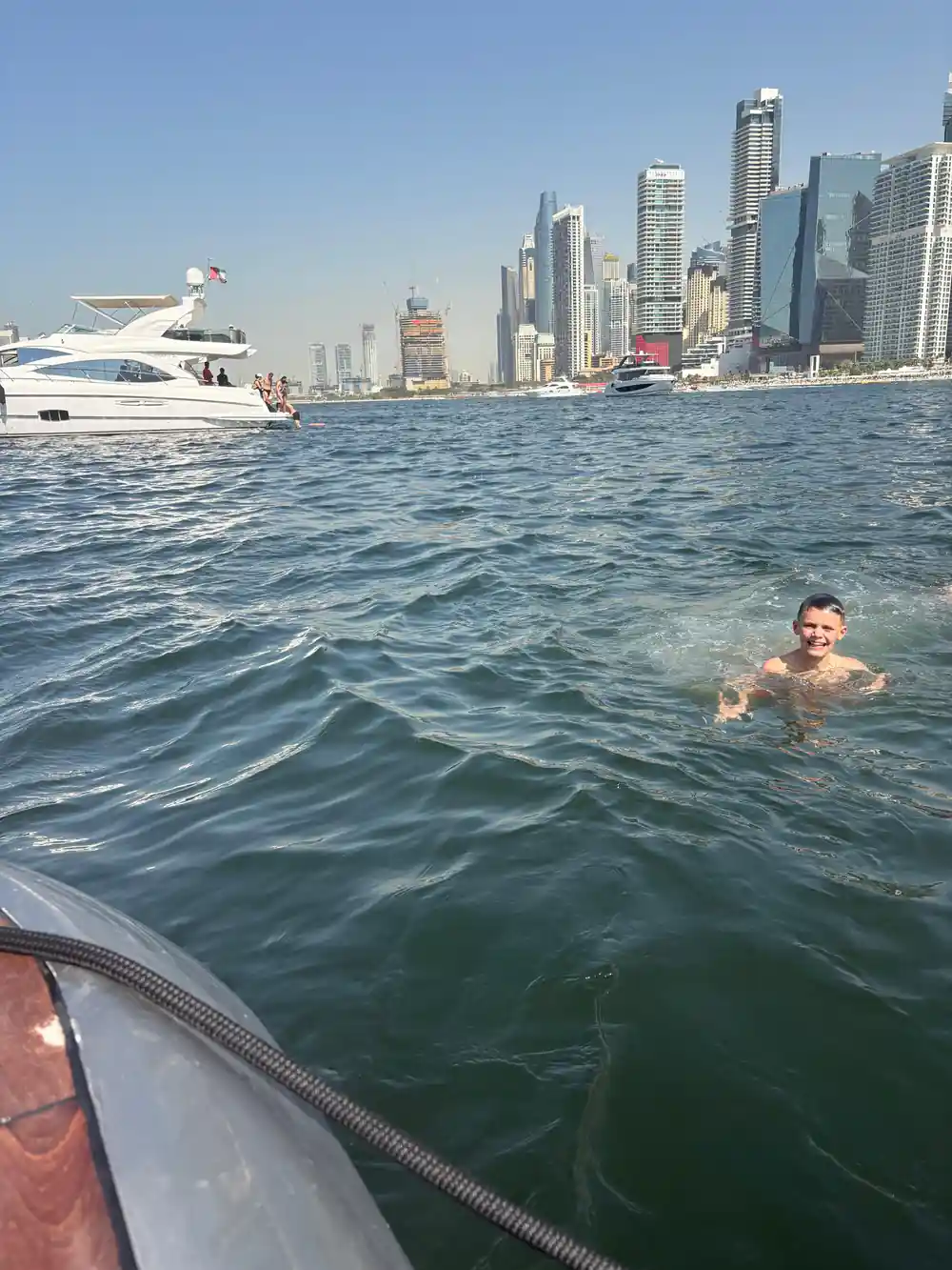 A swimmer in the water with the yacht and skyline beyond