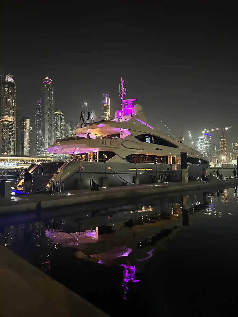 A yacht lit purple at night against the Marina skyline