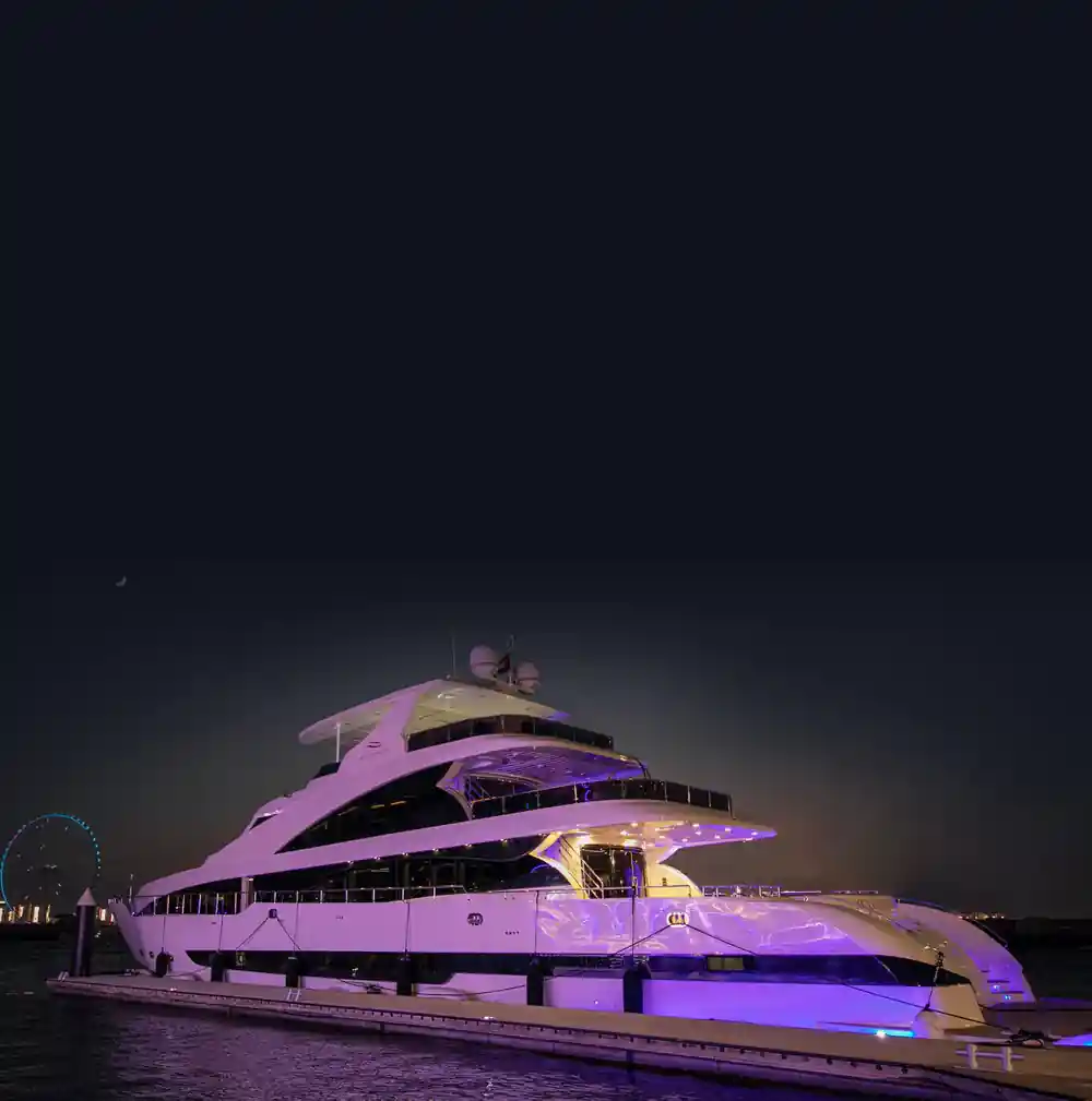The yacht lit purple at night against the marina