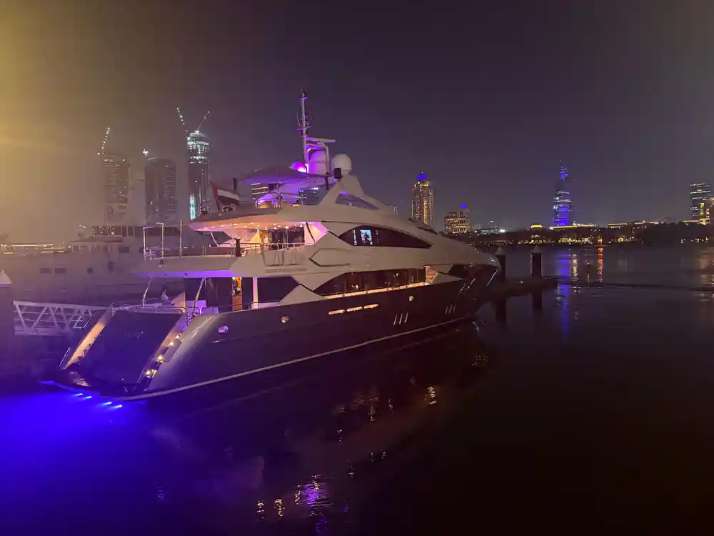 A yacht lit purple at night with towers behind